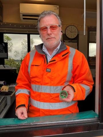 Person in an orange high-visibility jacket holding a coin.