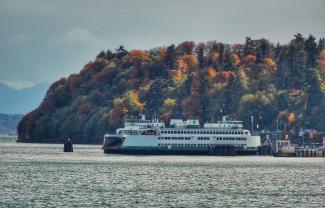 A washington state ferry on a body of water surrounded by colorful fall trees.