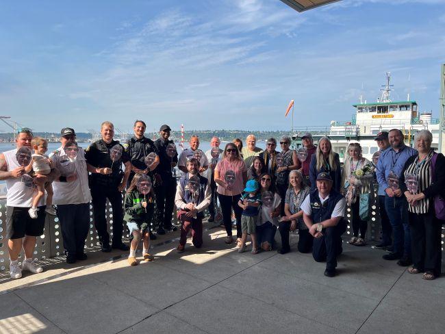 A group of people smiling and posing on a waterfront deck with a ferry in the background.