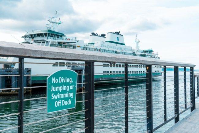 A ferry docked at a pier with a sign in the foreground reading "No Diving, Jumping or Swimming Off Dock."