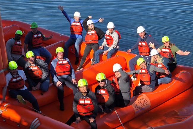 Group of people wearing safety gear on an orange inflatable raft in the water.