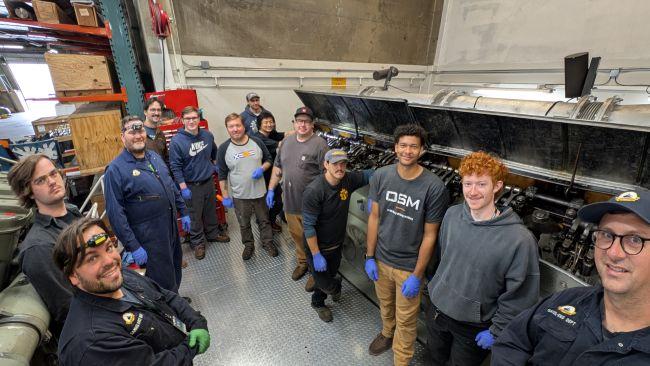 Group of people in a workshop setting with ferry engine machinery and industrial decor.